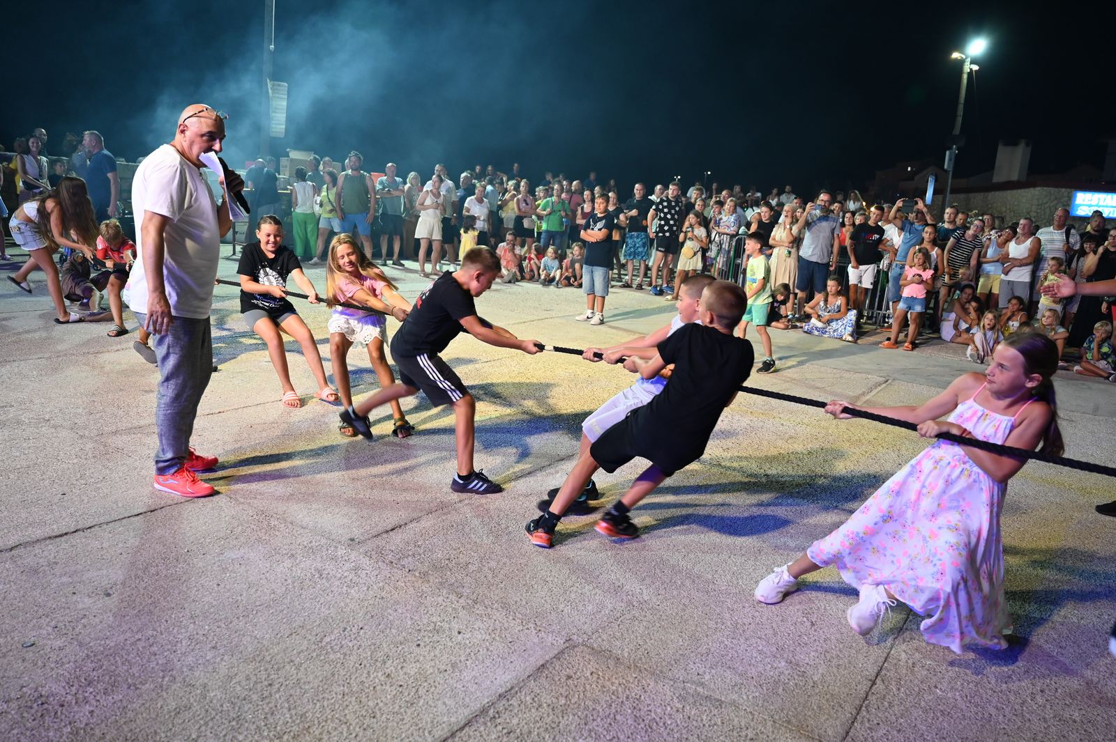 Noćna panorama manifestacije uz more: mnoštvo posjetitelja ispred osvijetljene pozornice